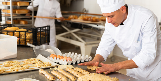 Boulanger-chapo.jpeg (Male baker working with dough forming baguettes)