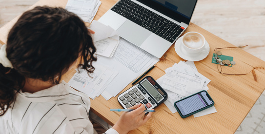 Gestion-chapo.jpeg (Top view of a woman working at home in the kitchen with financial papers, counting on a calculator, paying bills, planning a budget to save some money. Independent accounting, remote accountant)